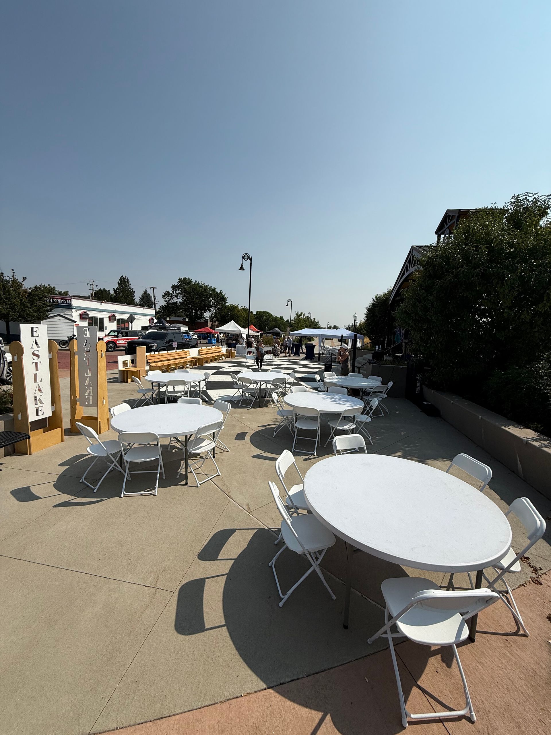 Outdoor patio with white round tables and chairs under a clear blue sky.