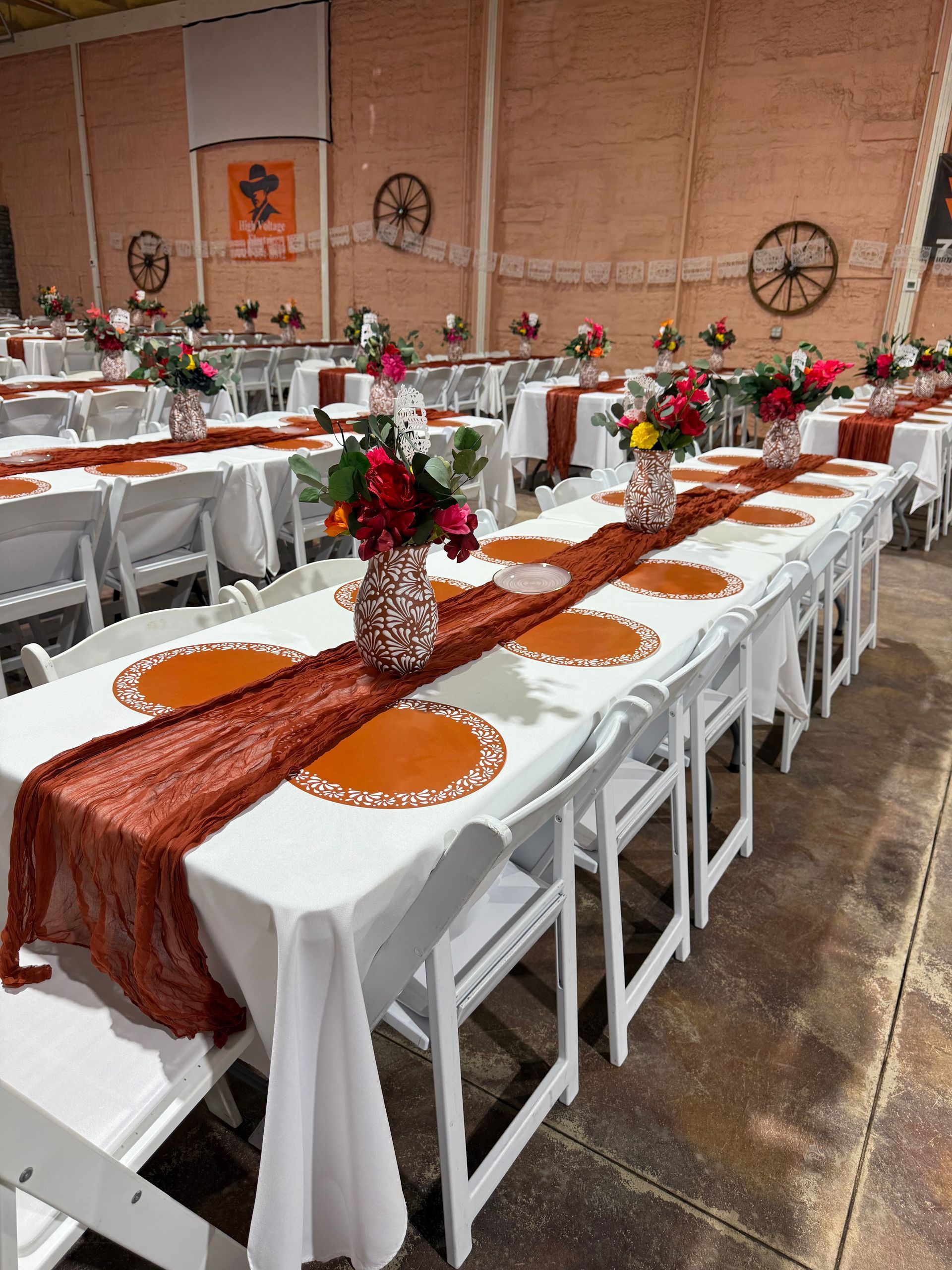 Long tables set for a banquet with white tablecloths, orange runners, and floral centerpieces.