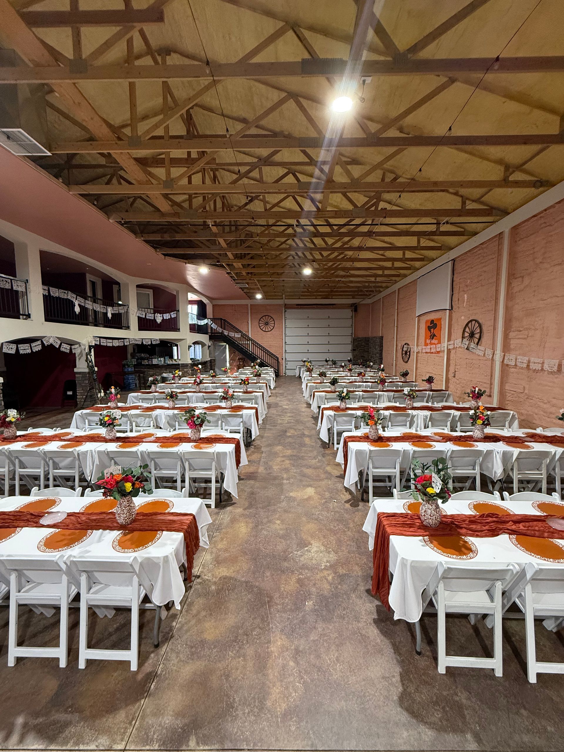 Large event space set up with rows of white tables, rust-colored runners, and floral centerpieces.