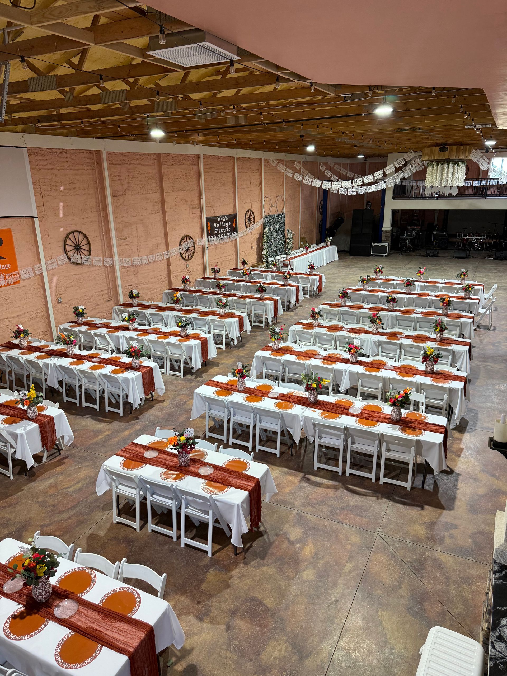 Large event space with rows of tables set with orange and white linens, likely for a gathering.