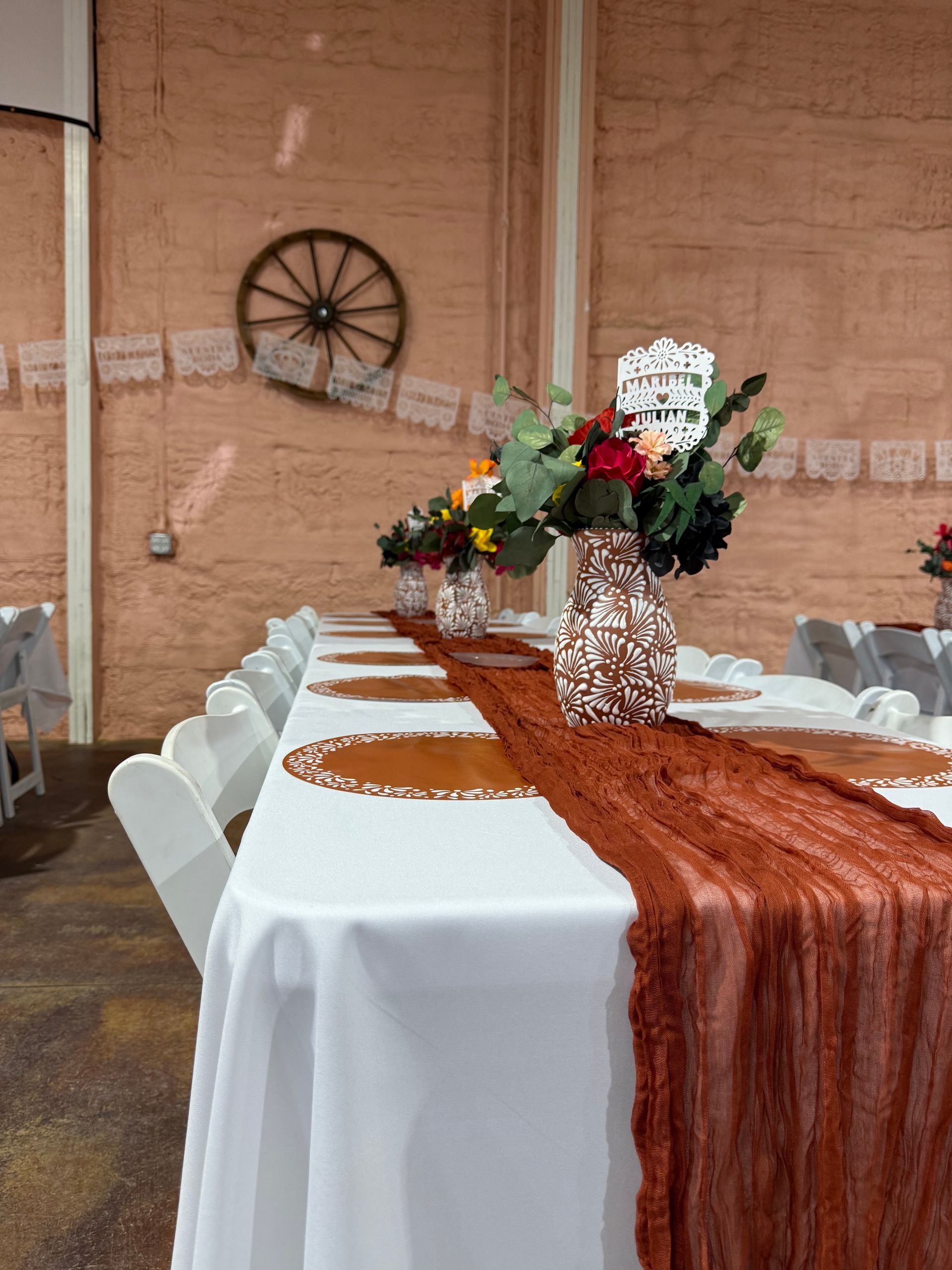Long table with white tablecloth, decorated with flowers and orange runner.