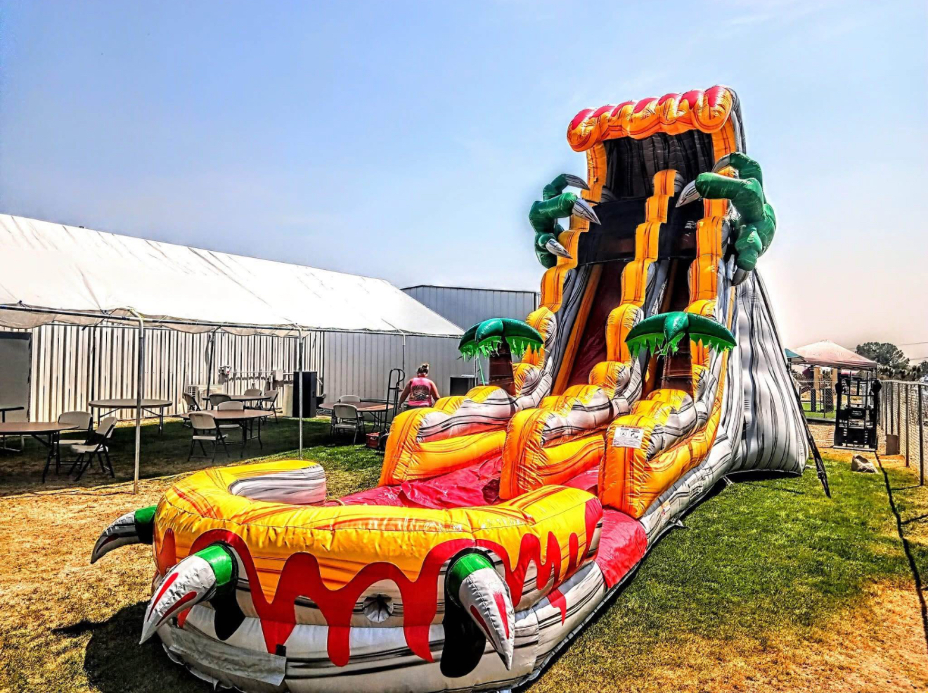 Inflatable volcano water slide on a grassy field with event tents in the background.