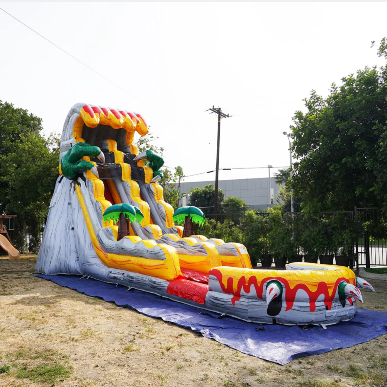 Inflatable water slide shaped like a volcano with palm trees. Grey, yellow, red, and brown colors.