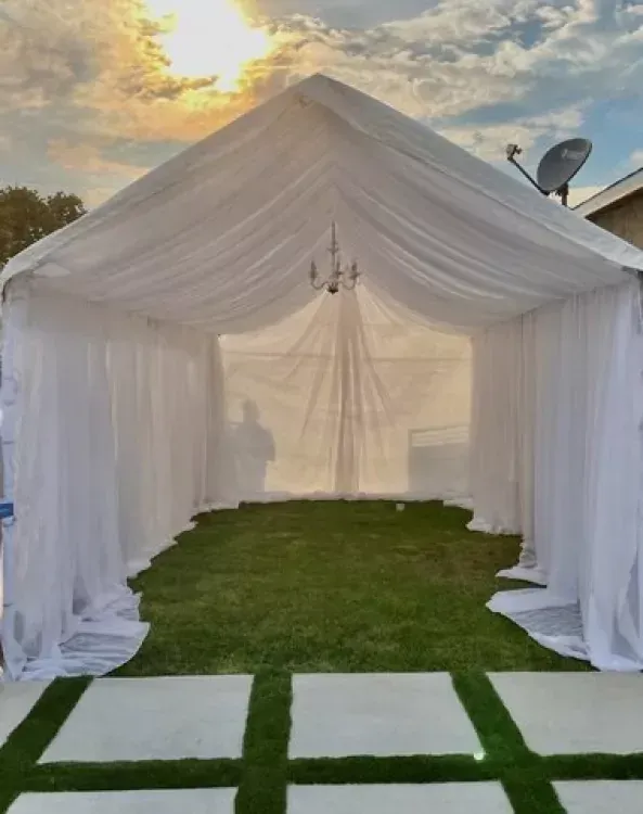 White tent draped with fabric over green grass, a chandelier inside; outdoors.
