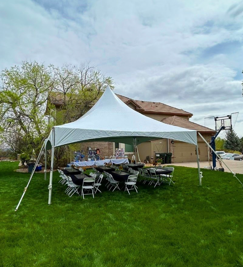 White tent set up in a backyard with tables, chairs, and decorations. Cloudy sky.