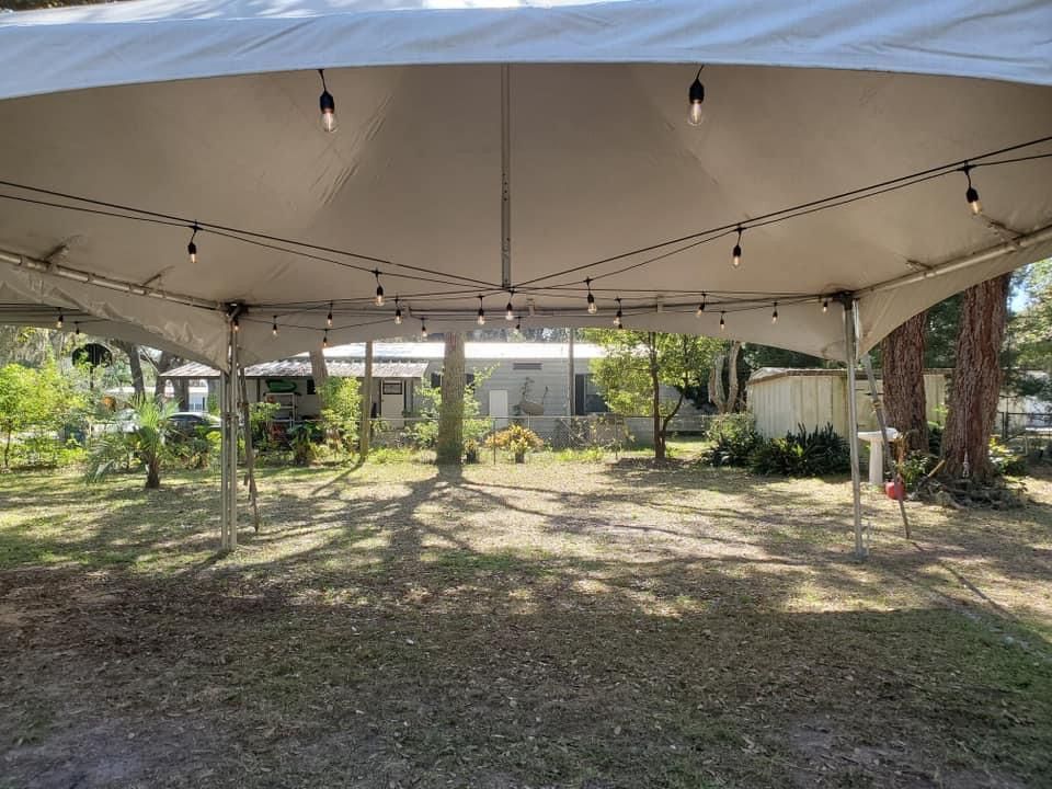 Inside a white tent, looking out at a grassy yard and building. String lights hang from the tent ceiling.