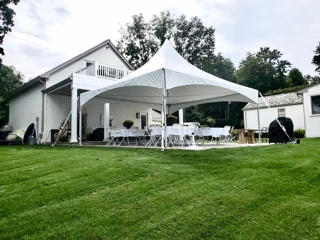White tent set up in a backyard next to a house, with tables and chairs set up under the tent.