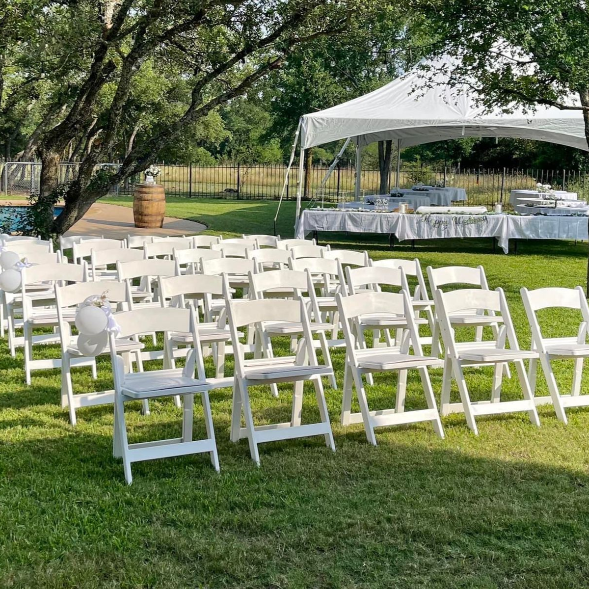 White chairs arranged outdoors, tent and food setup in background, sunny day.