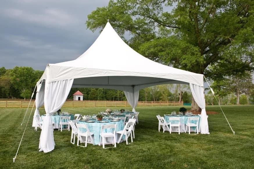 White tent set up with tables and chairs on a grassy lawn.