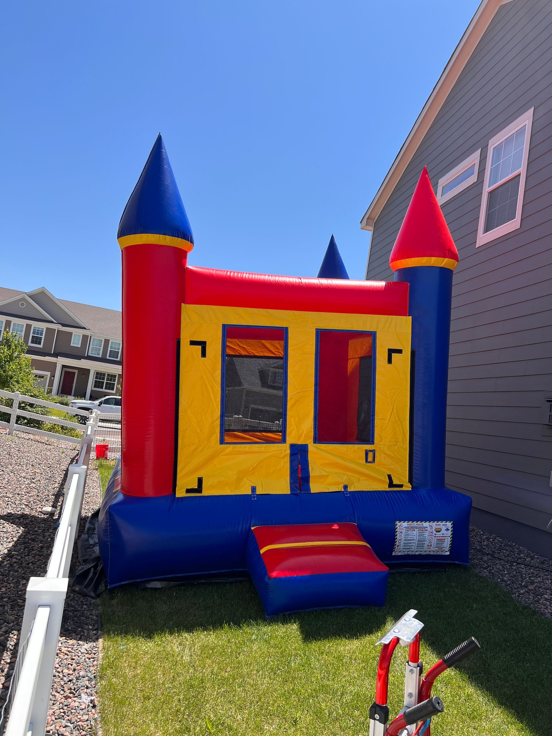 Colorful inflatable bounce house with castle turrets on green grass near a house.