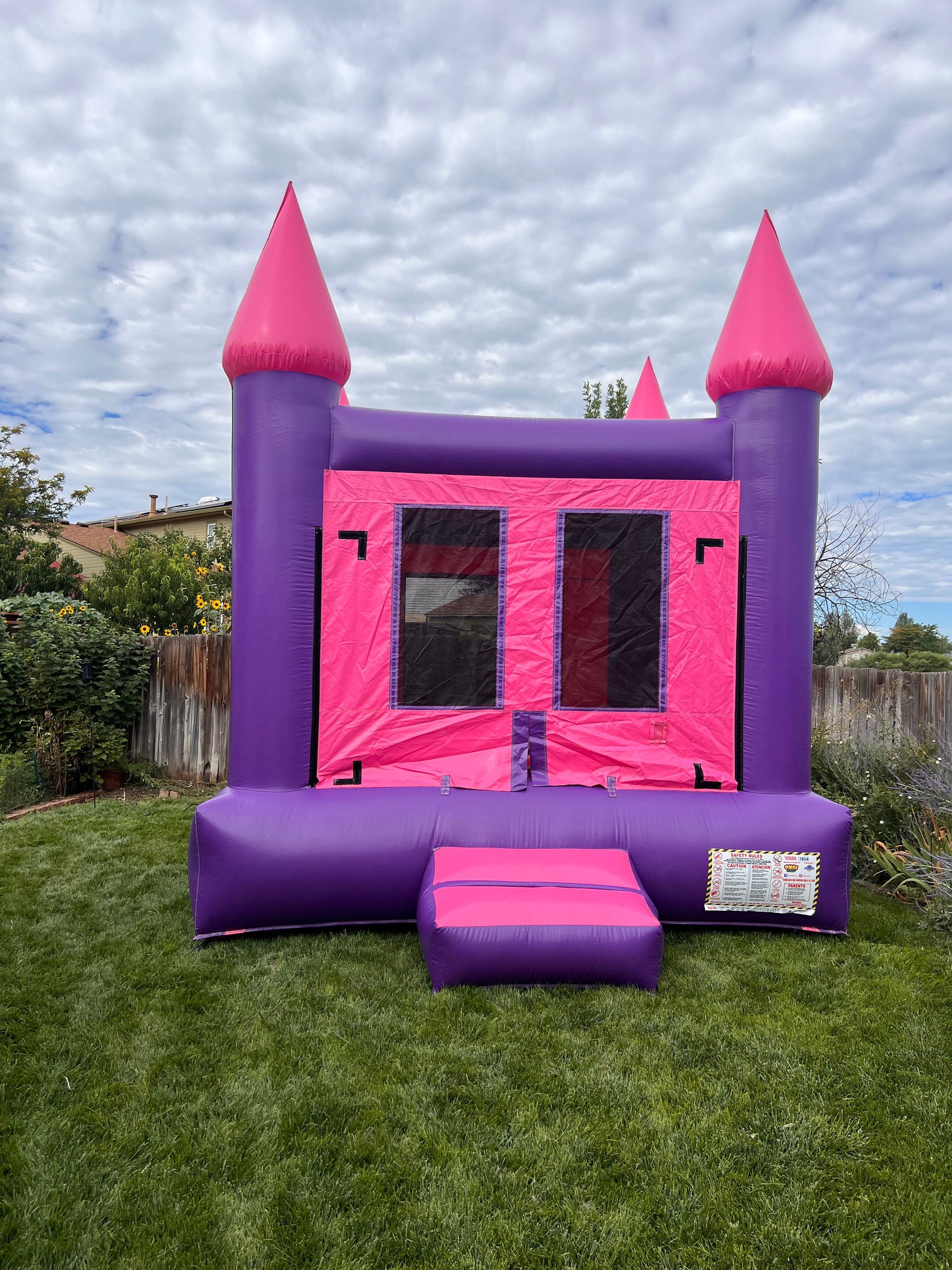 Purple and pink inflatable bouncy castle on green grass in a backyard.