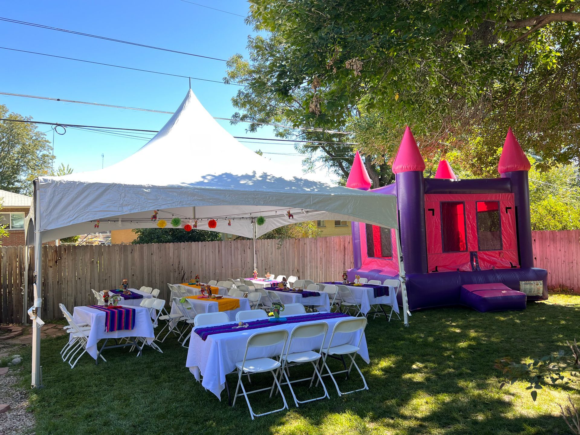 Backyard party setup with a tent, tables, chairs, and a pink and purple bounce house.