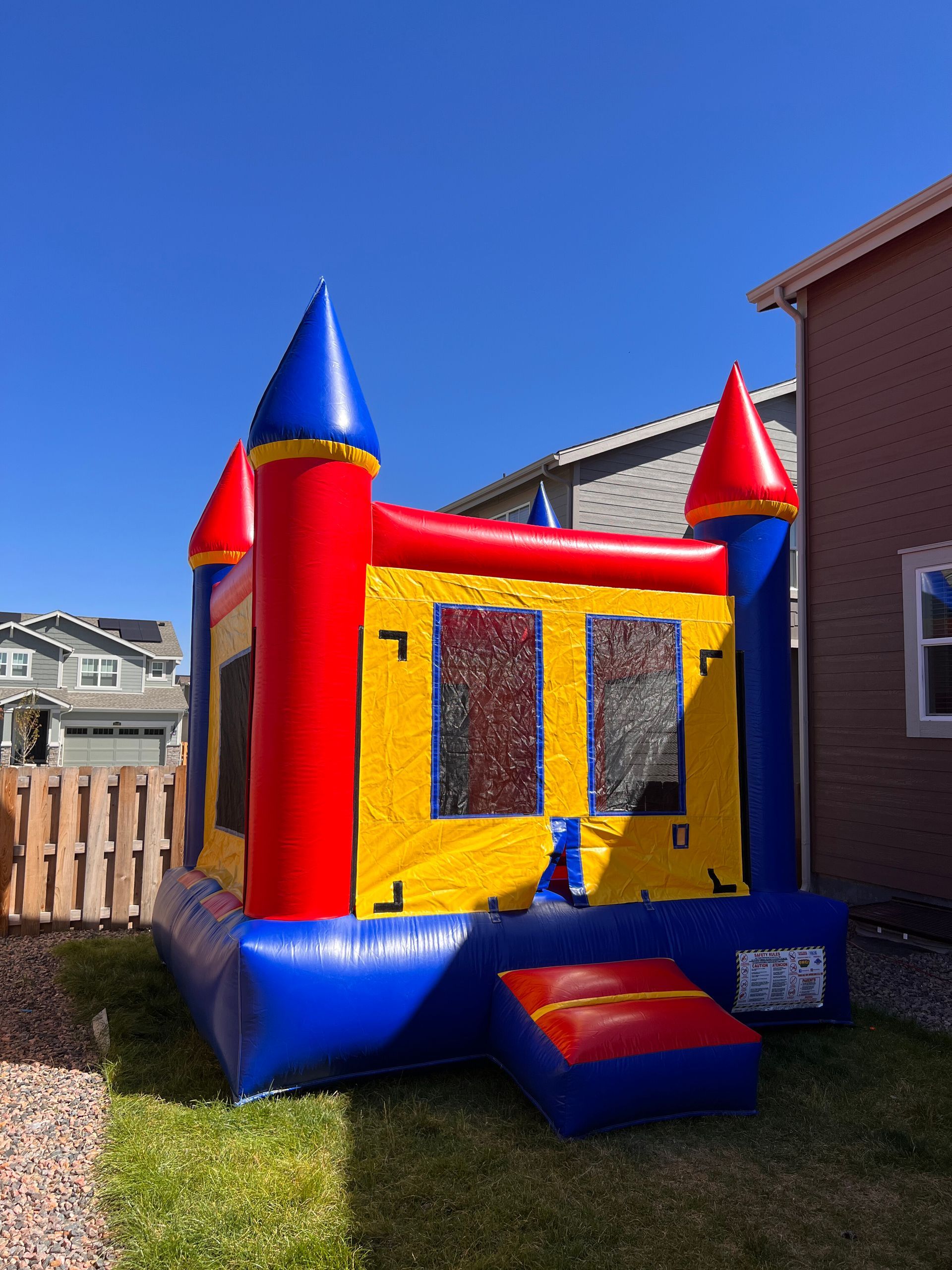 A colorful inflatable castle bounce house on green grass under a blue sky.