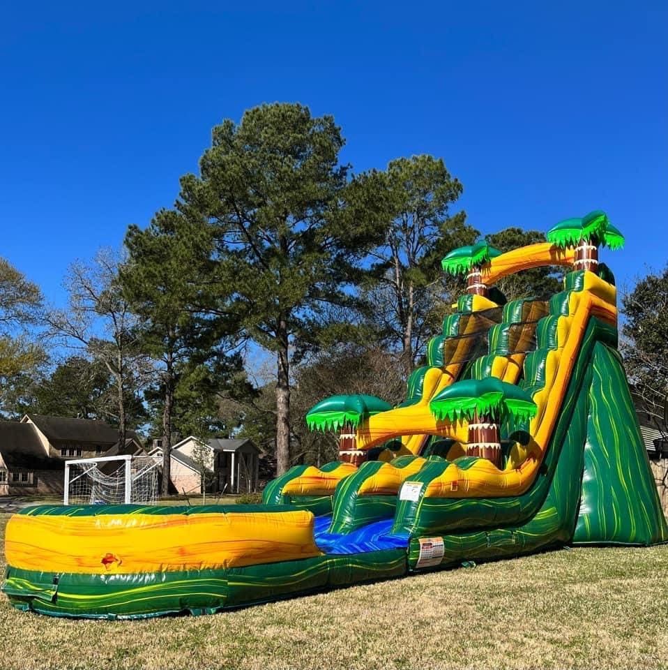 Green and yellow inflatable water slide with palm tree decorations in a yard.