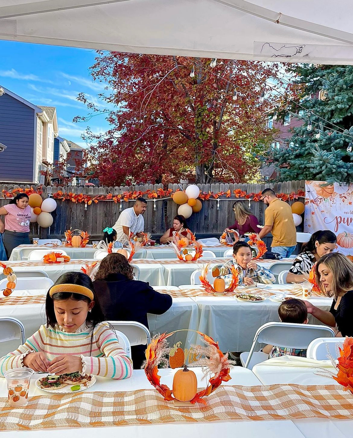 Outdoor party with decorated tables, autumn colors, and people.