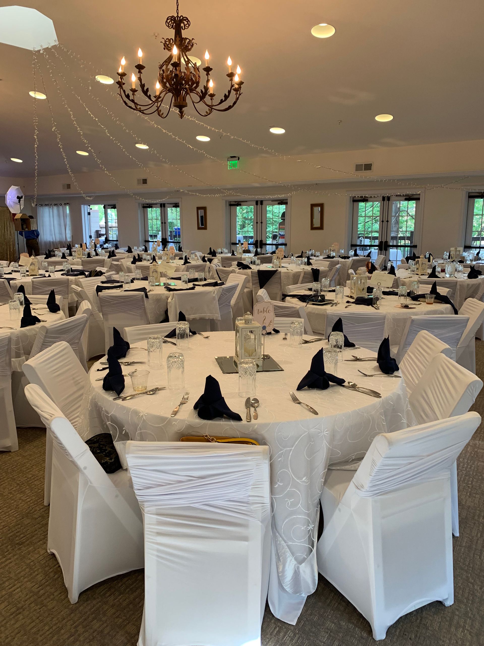 Ballroom set for an event with round tables, white tablecloths, black napkins, and chair covers.