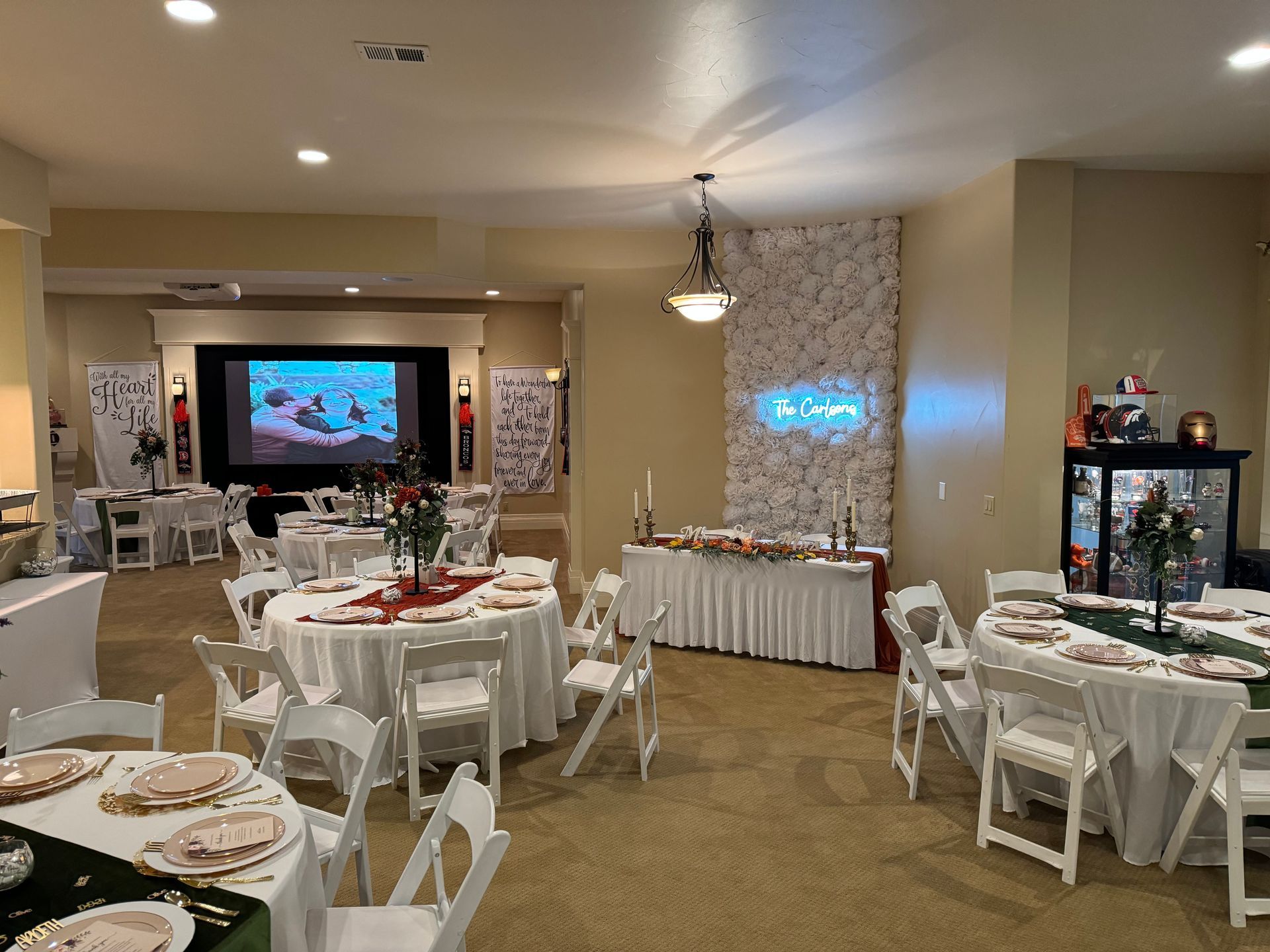 Event room set with round tables, white chairs, and decorative floral backdrop.