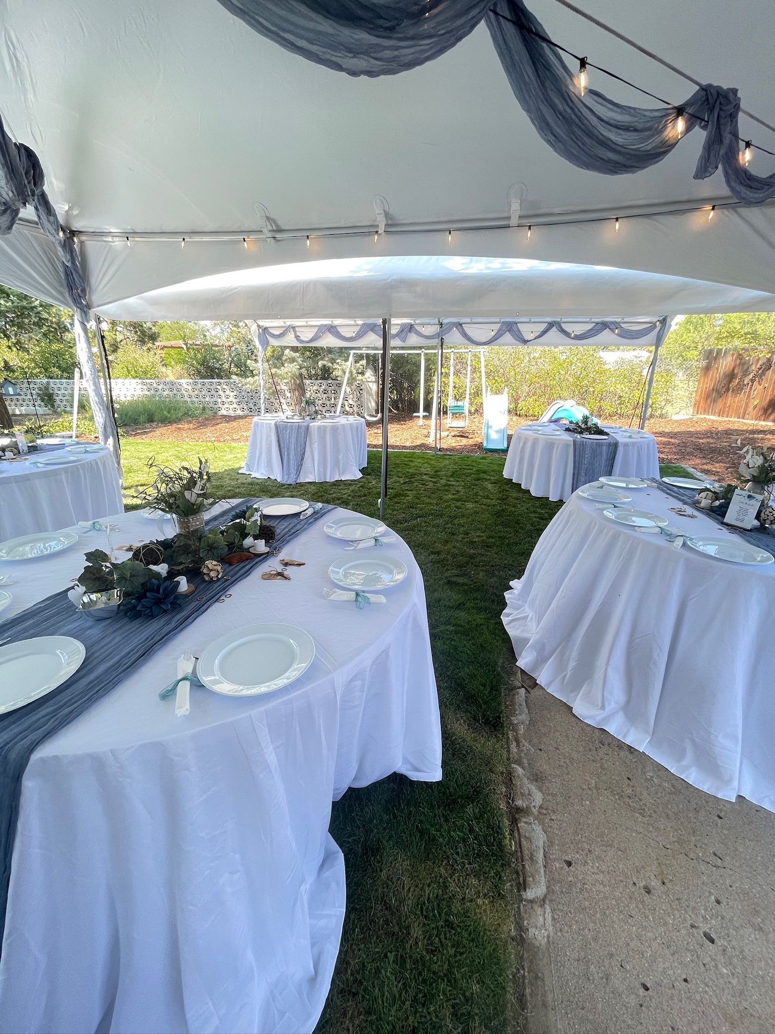 Wedding reception tent with tables set for guests; white linens, blue runners, floral centerpieces.