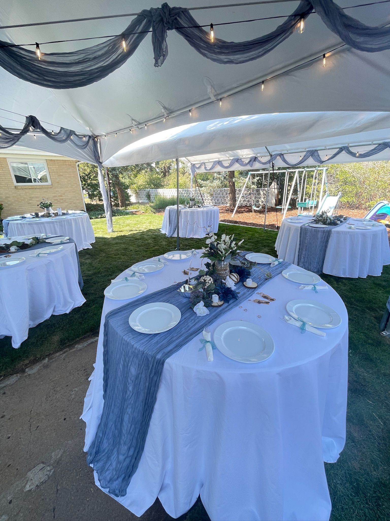 Wedding reception tables under a white tent, decorated with blue runners and flowers.