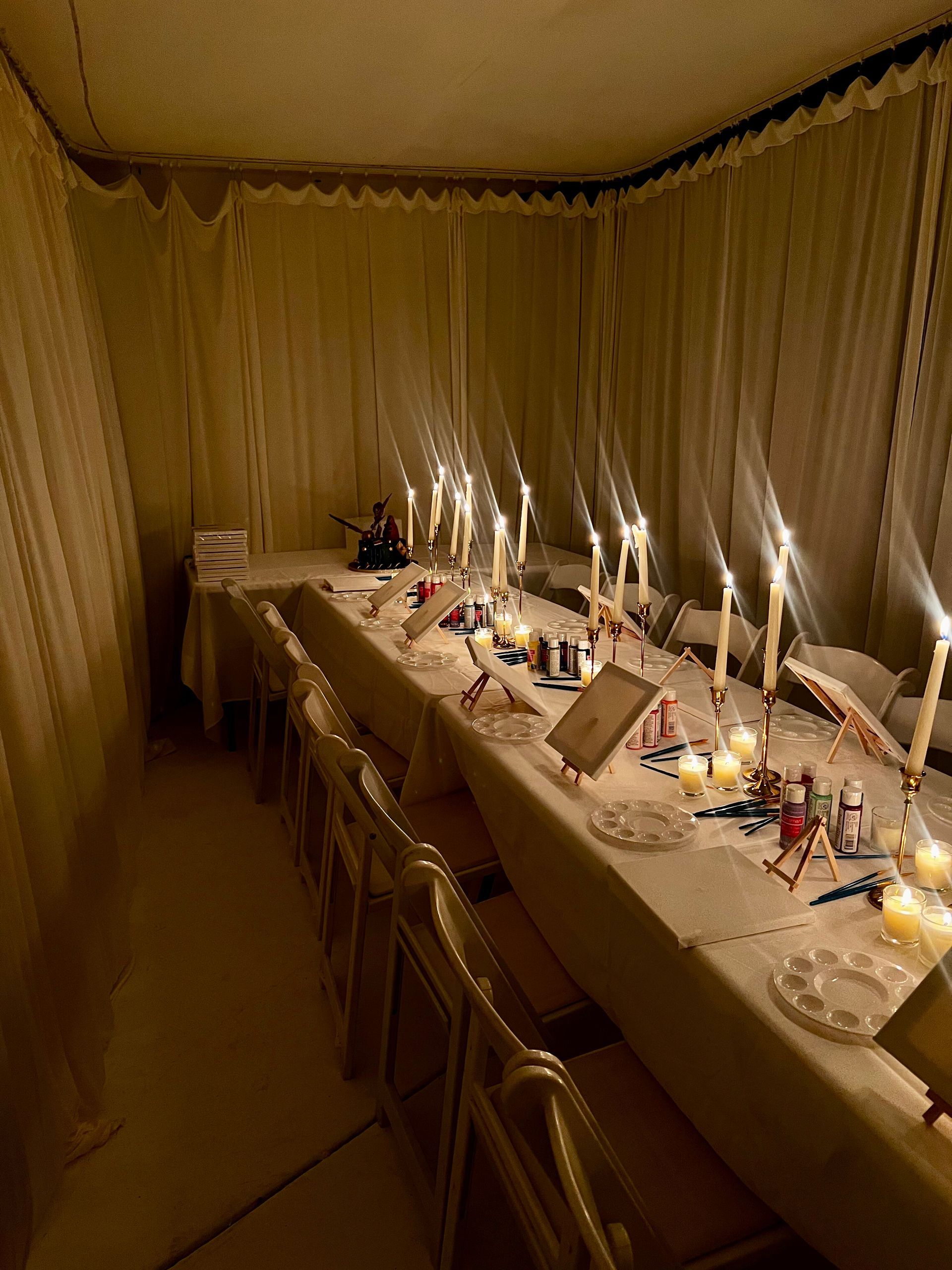 Long table set with candles and place settings in a softly lit room with sheer curtains.
