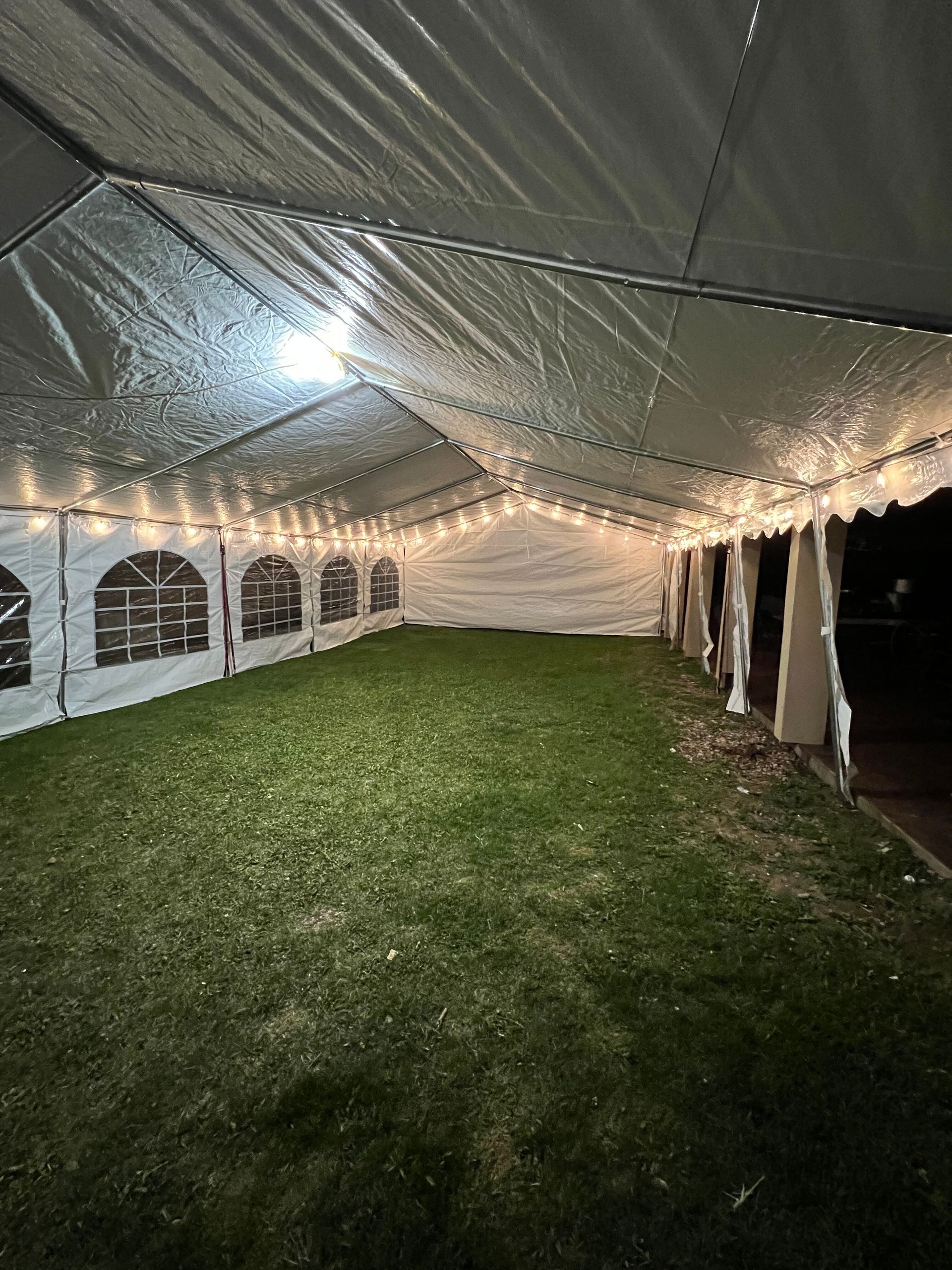 Inside a white tent, string lights illuminate the green grass.