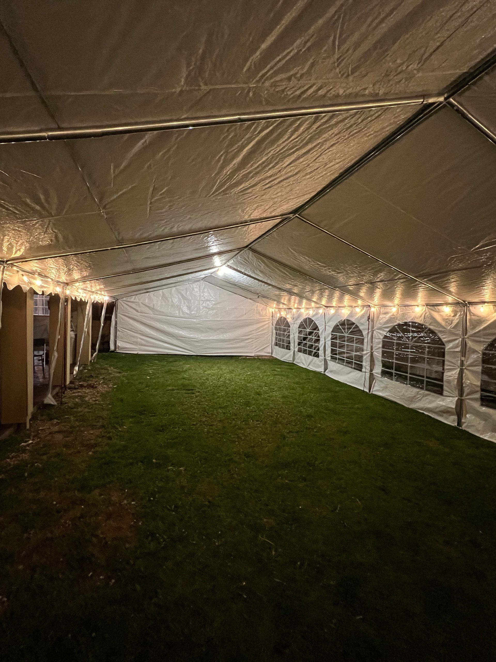 Inside a white party tent, lit with string lights, on green grass.
