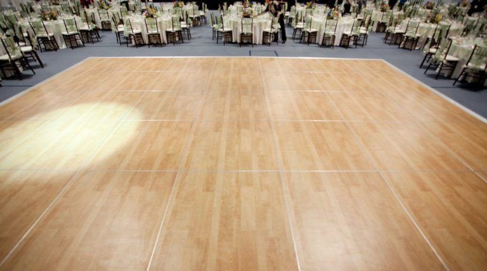 A large wooden dance floor in a ballroom, surrounded by tables with white tablecloths and chairs.
