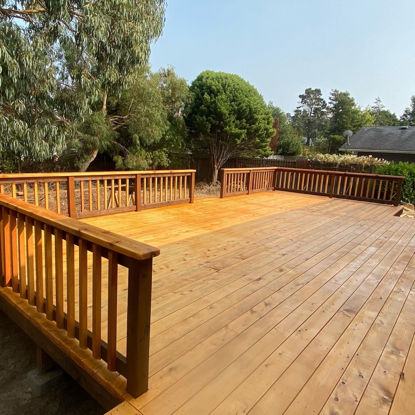 Wooden deck with railing in a backyard setting, trees in background, sunny day.