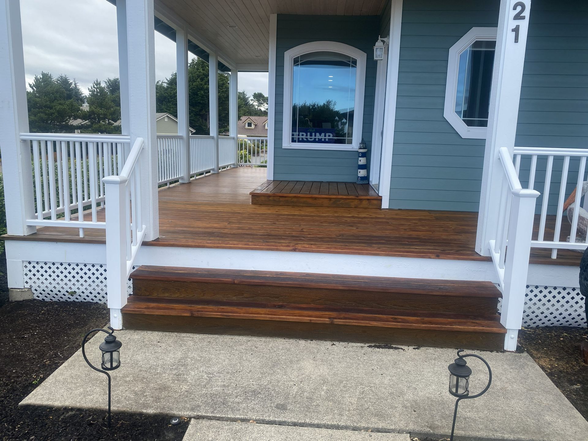 Exterior of a house with a porch. Teal siding, white railings, and brown wooden deck.