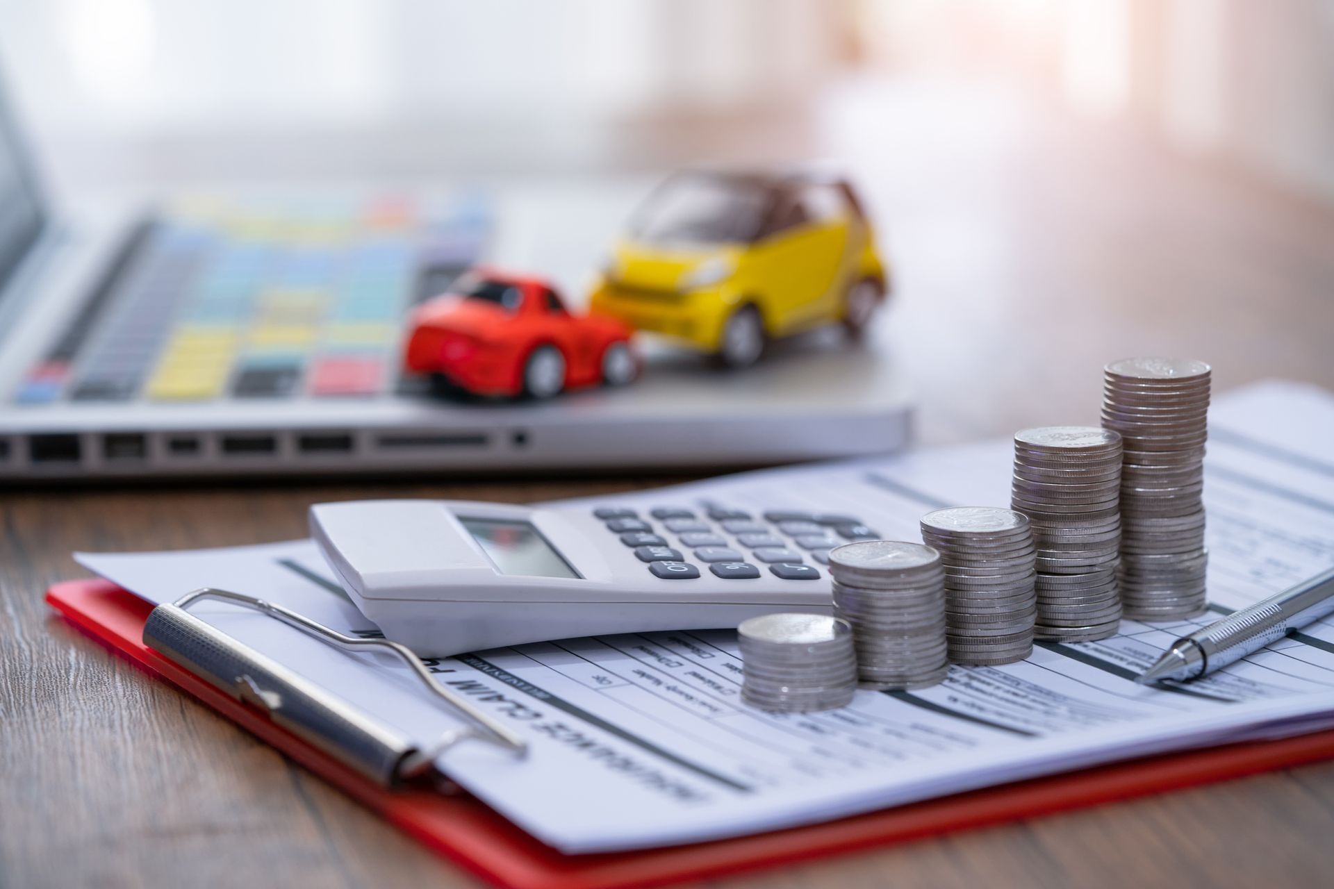 Stacks of coins on financial documents with calculator, pen, and toy cars.