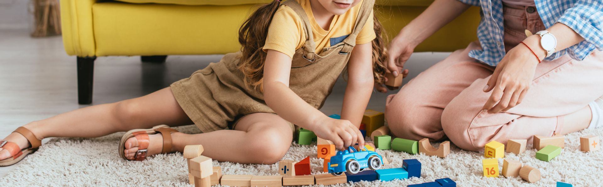 A woman and a child are sitting on the floor playing with wooden blocks.
