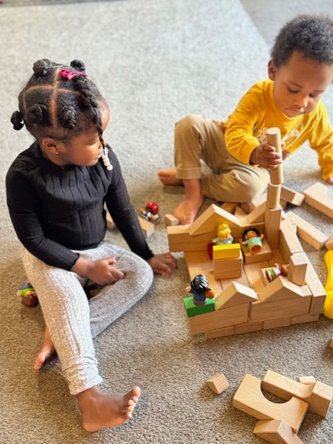 A boy and a girl are playing with wooden blocks on the floor.