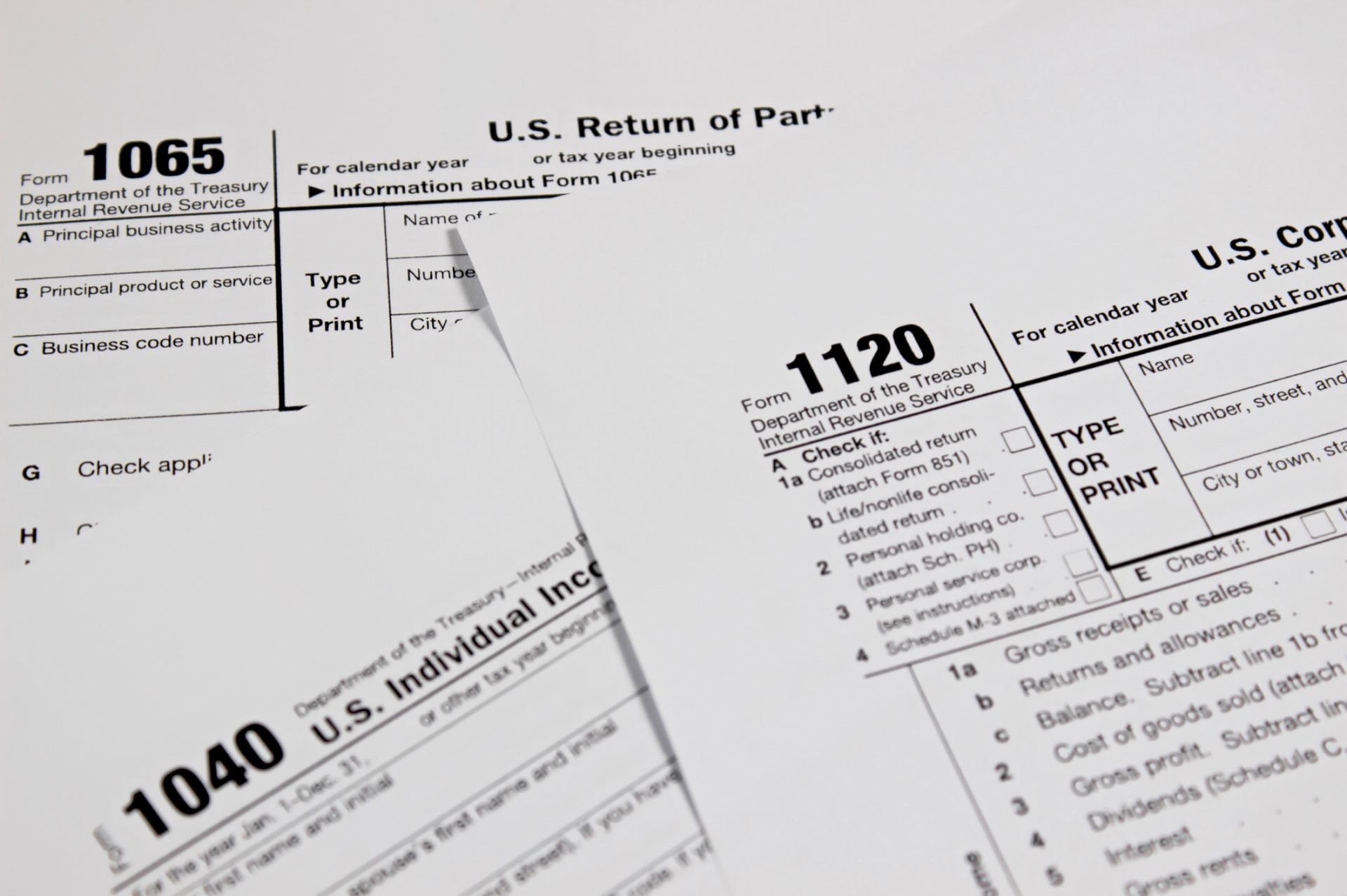Tax forms: 1065, 1120, and 1040 are stacked. The forms are white.