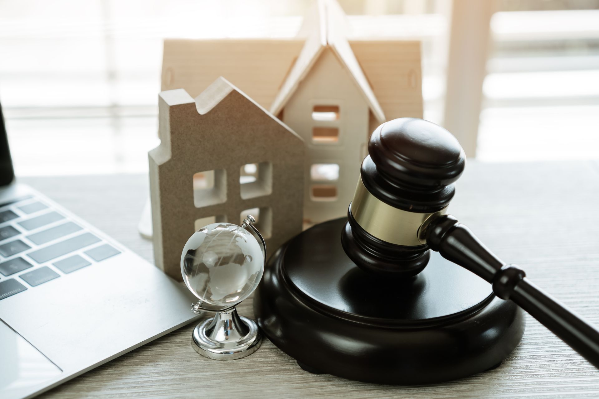 Wooden house model, gavel, globe, and laptop on a table, representing legal or real estate matters.