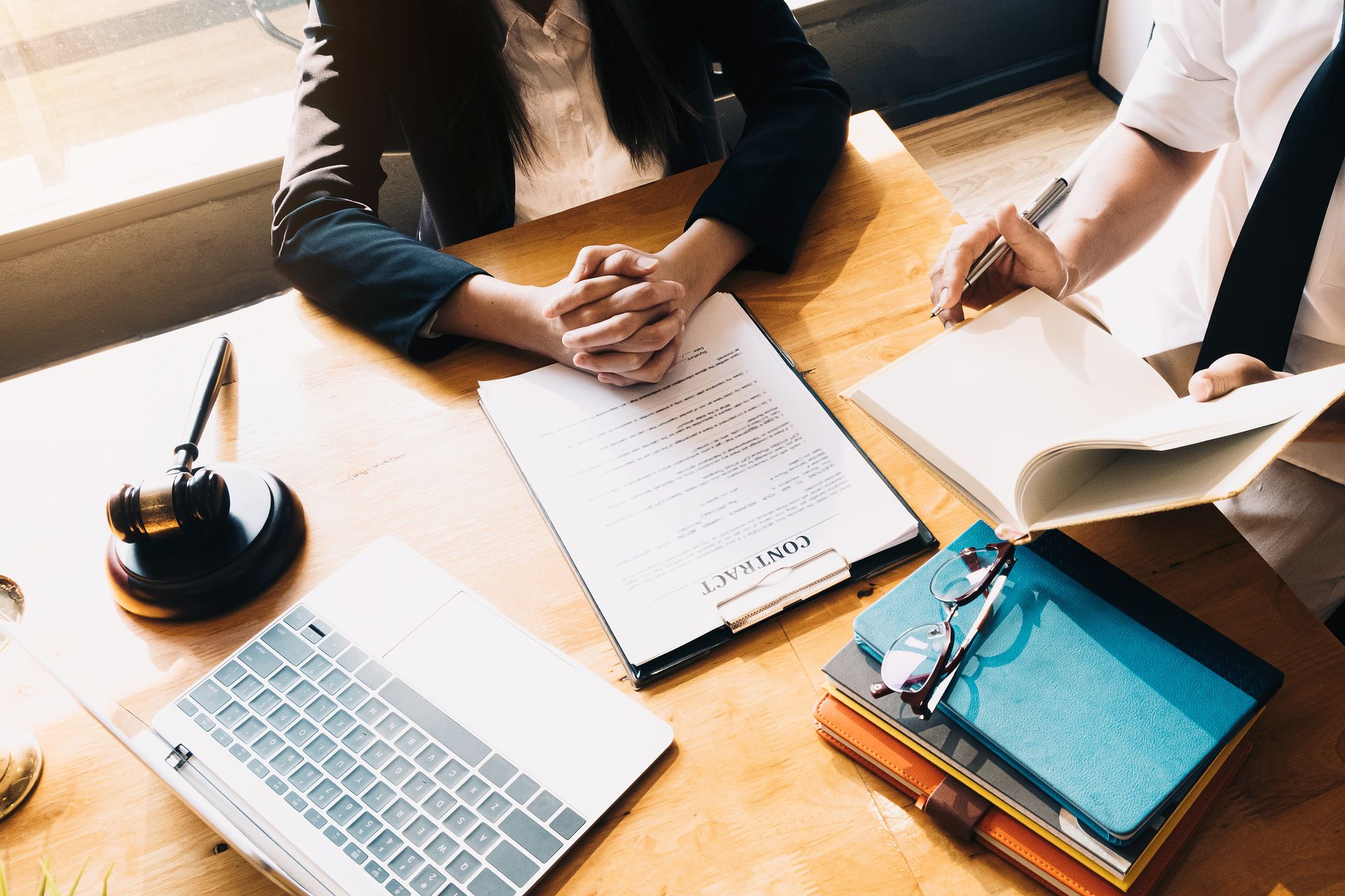 People reviewing contract and legal documents at a desk; includes gavel, laptop, and books.
