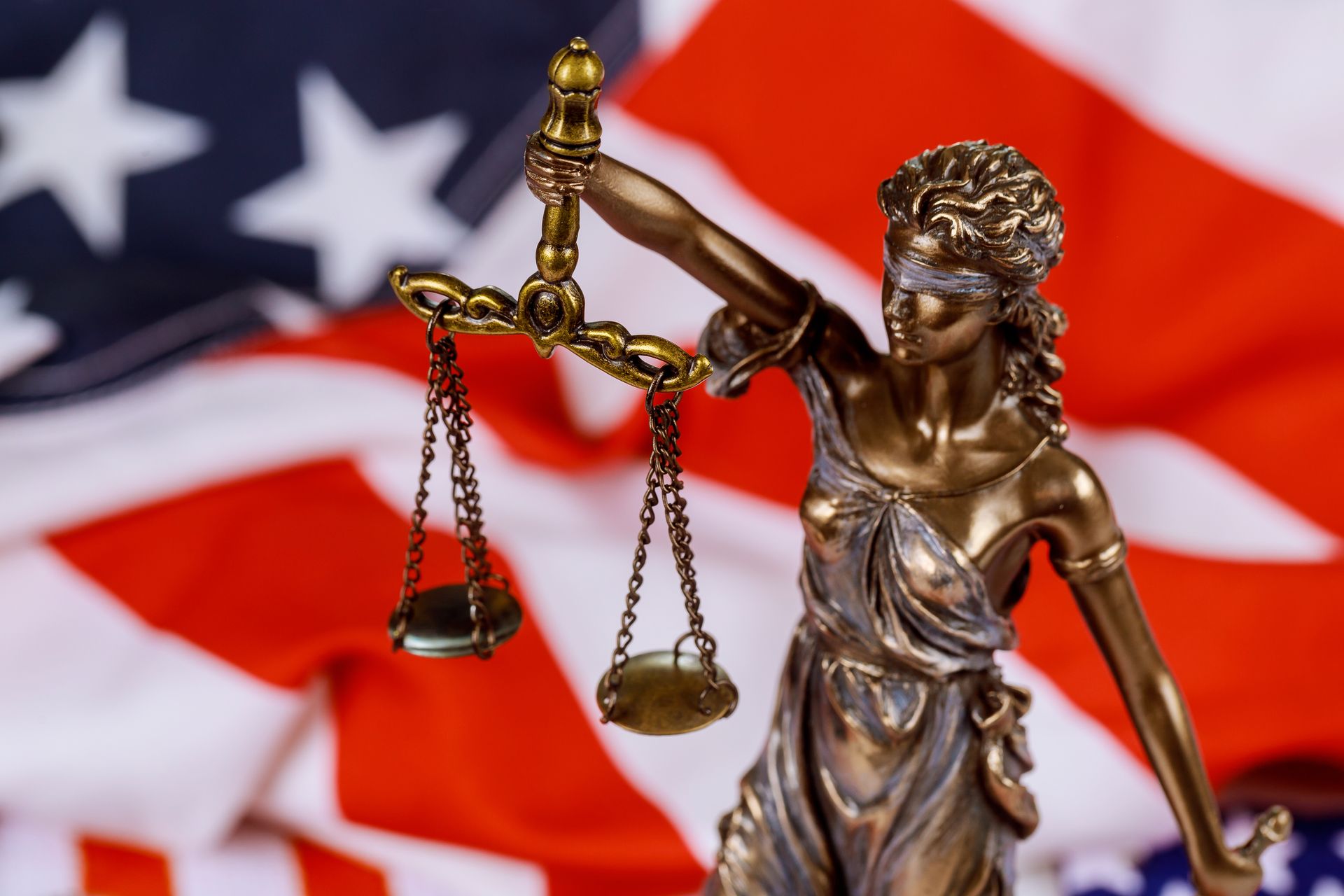 Statue of Lady Justice holding scales, blindfolded, with American flag background.