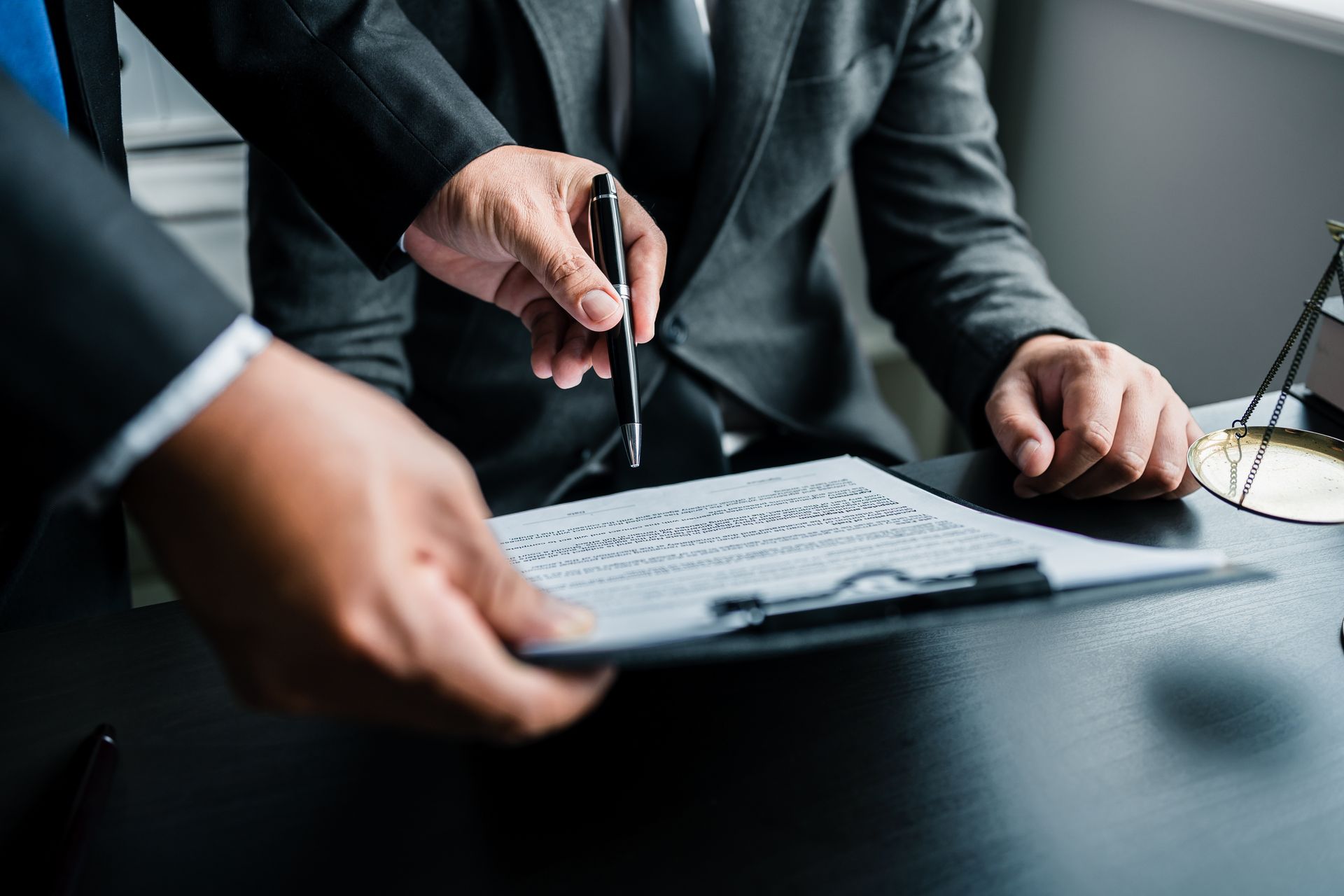 Two people in suits examining a document on a clipboard. One points with a pen.