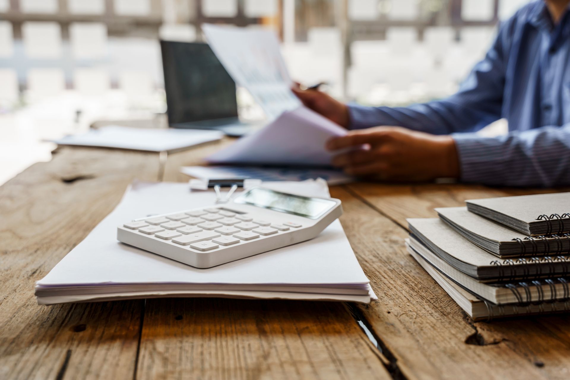 Person reviewing documents at a desk, calculator and notebooks in foreground.