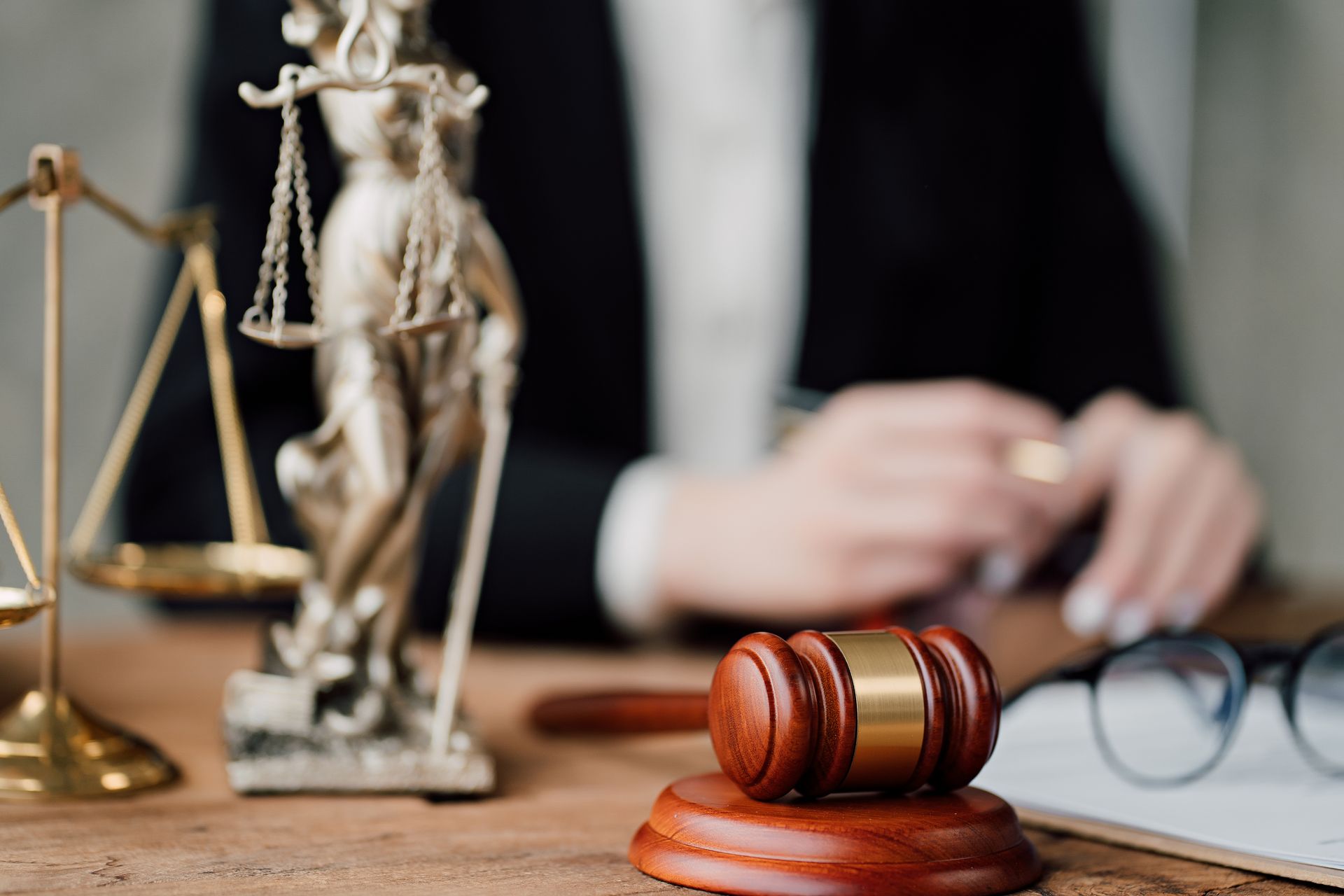 Gavel and scales of justice on a desk with a person in a blazer in the background.