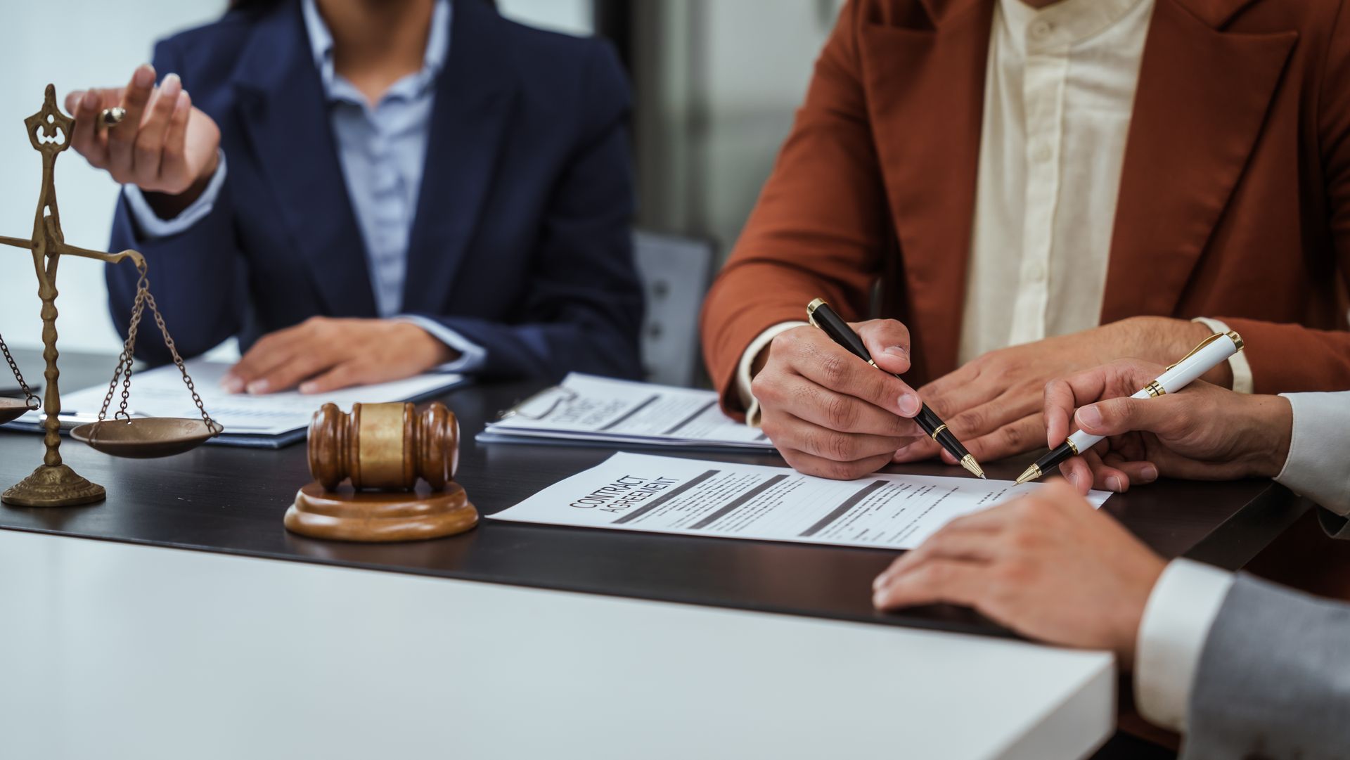 Lawyers at a table reviewing documents, signing a form. Scales of justice, gavel present.