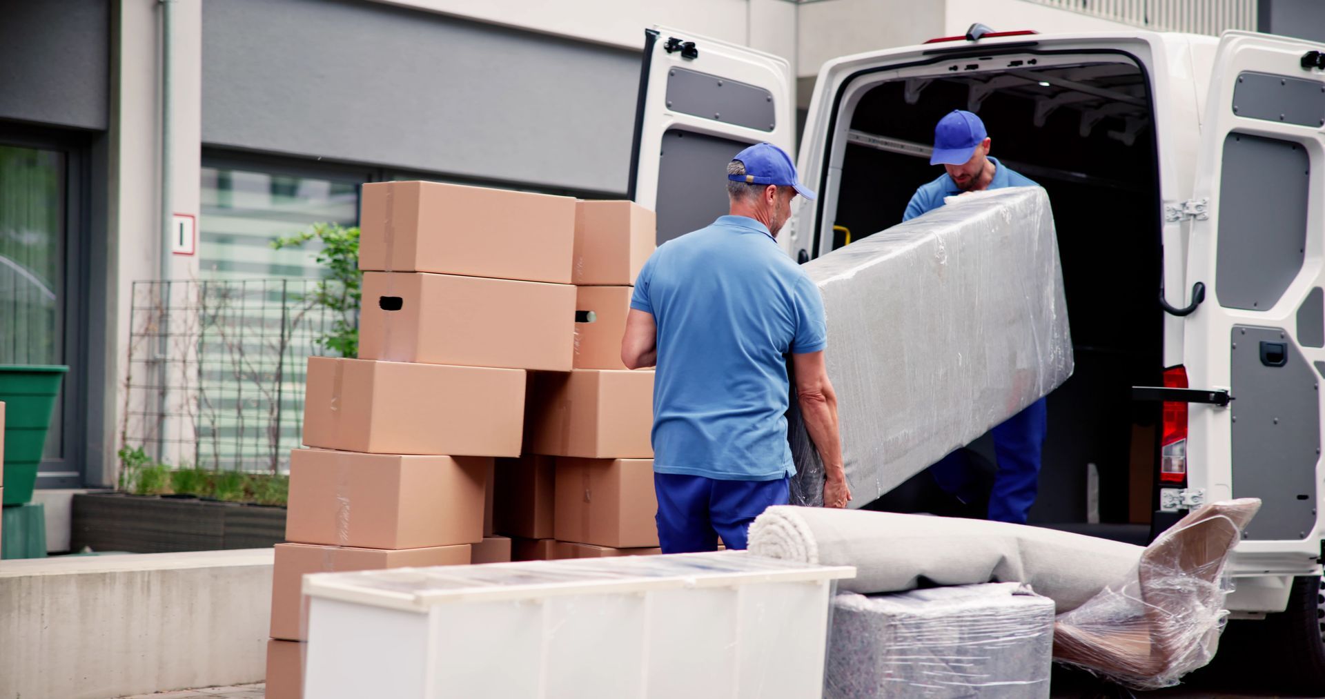 Workers loading boxed goods into a delivery van beside a warehouse loading dock