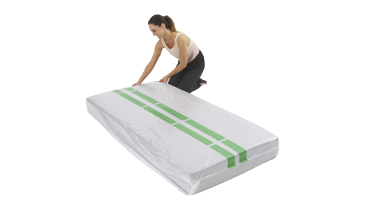 Woman kneeling, wrapping a mattress in clear plastic with green tape on a white background.