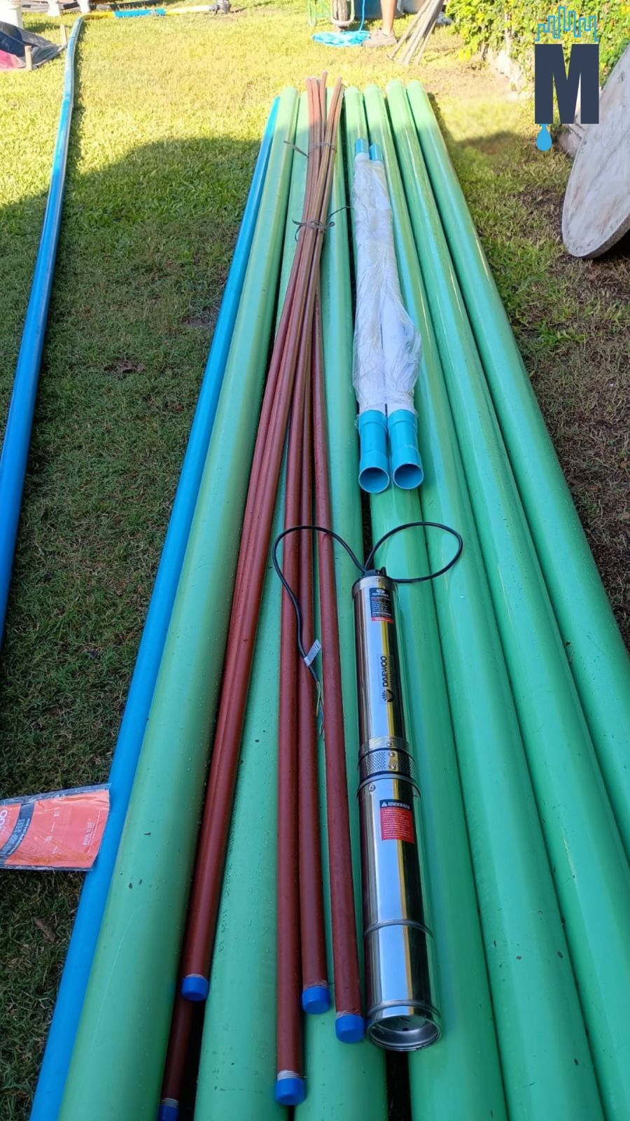 Tuberías de colores y un taladro metálico yacen sobre el césped en una zona de trabajo al aire libre.
