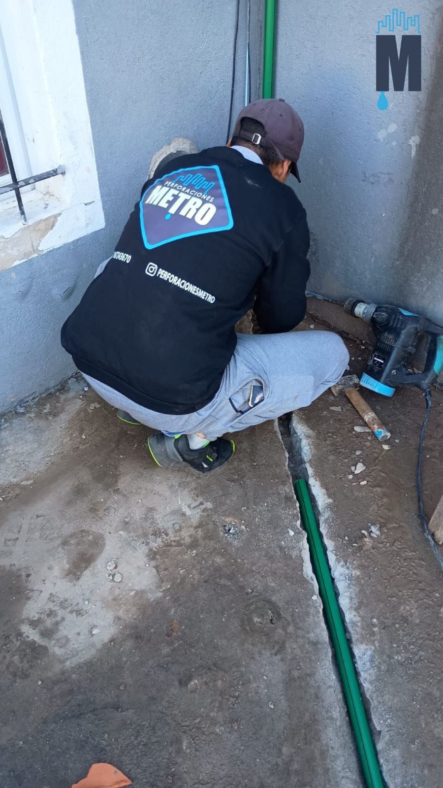 Técnico agachado junto a una pared, inspeccionando tuberías y herramientas en una pequeña área de servicio.