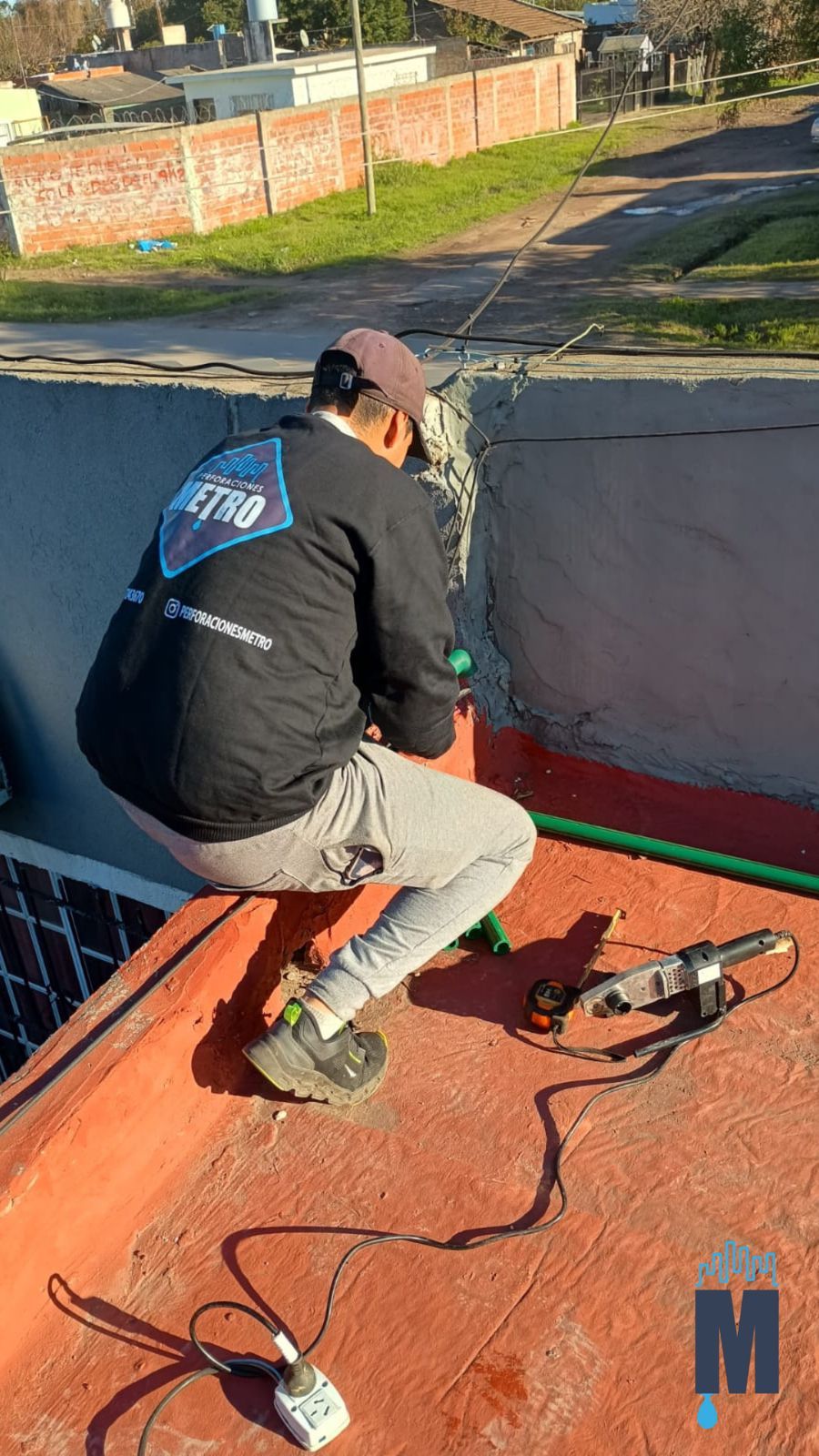 Un trabajador, arrodillado en una azotea, sella una membrana oscura a lo largo del borde con herramientas a mano.