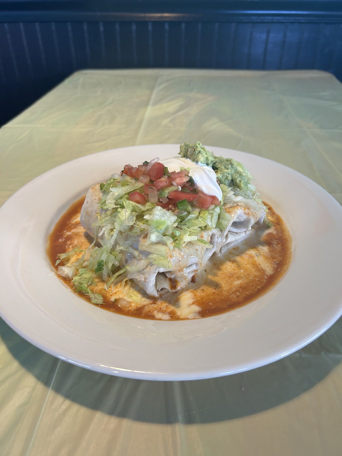 Burrito with red sauce, topped with lettuce, salsa, guacamole, and sour cream on a white plate.