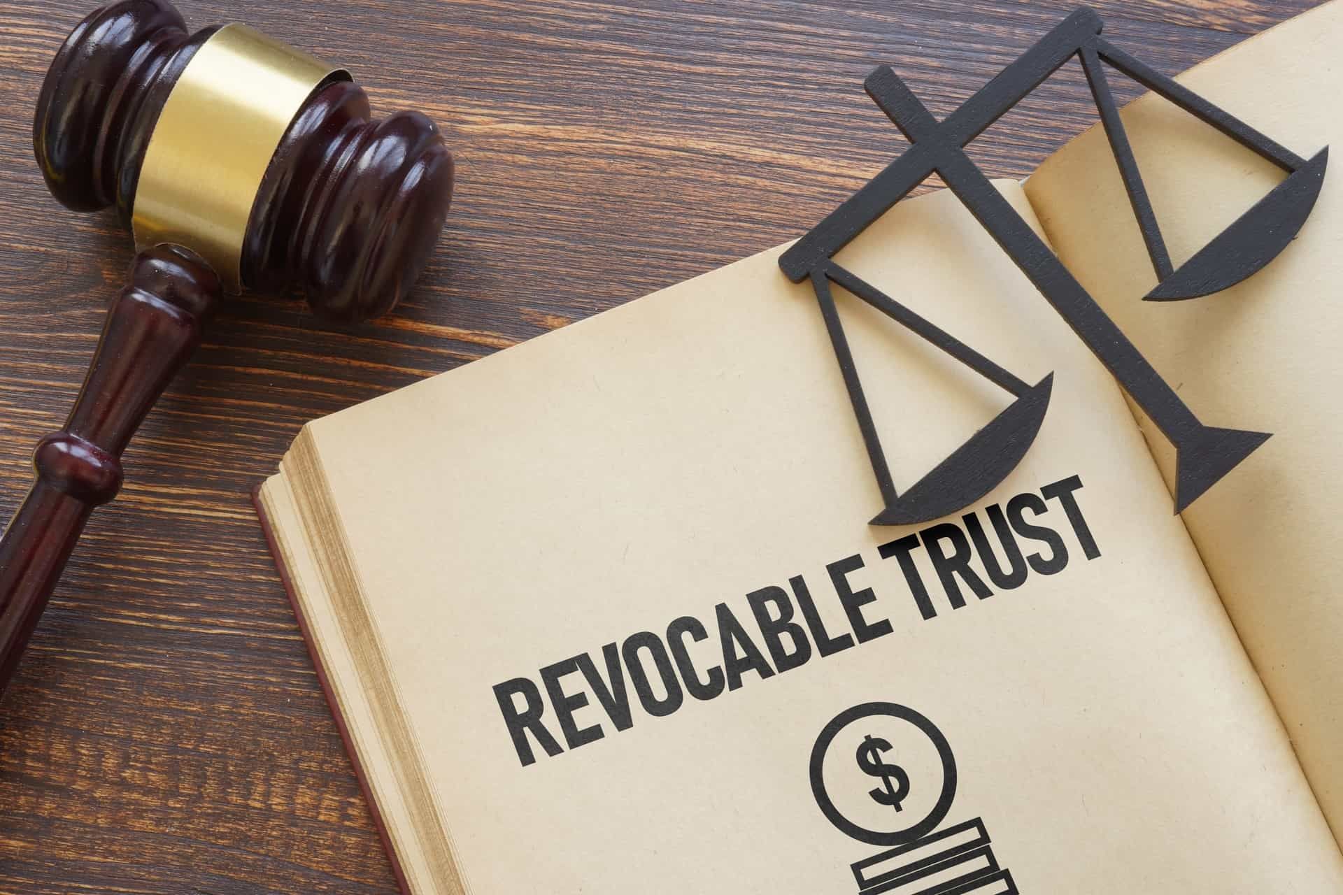 Gavel and scales of justice on an open book displaying "REVOCABLE TRUST," symbolizing estate planning and legal considerations for asset protection.