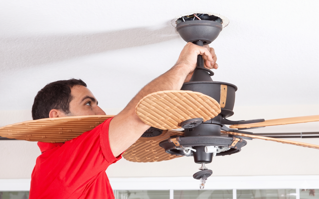 Man hanging a black geometric ceiling light fixture on a white ceiling