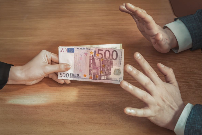 De ene persoon biedt een stapel bankbiljetten van 500 euro aan, terwijl een andere persoon met gebaren het aanbod afwijst.