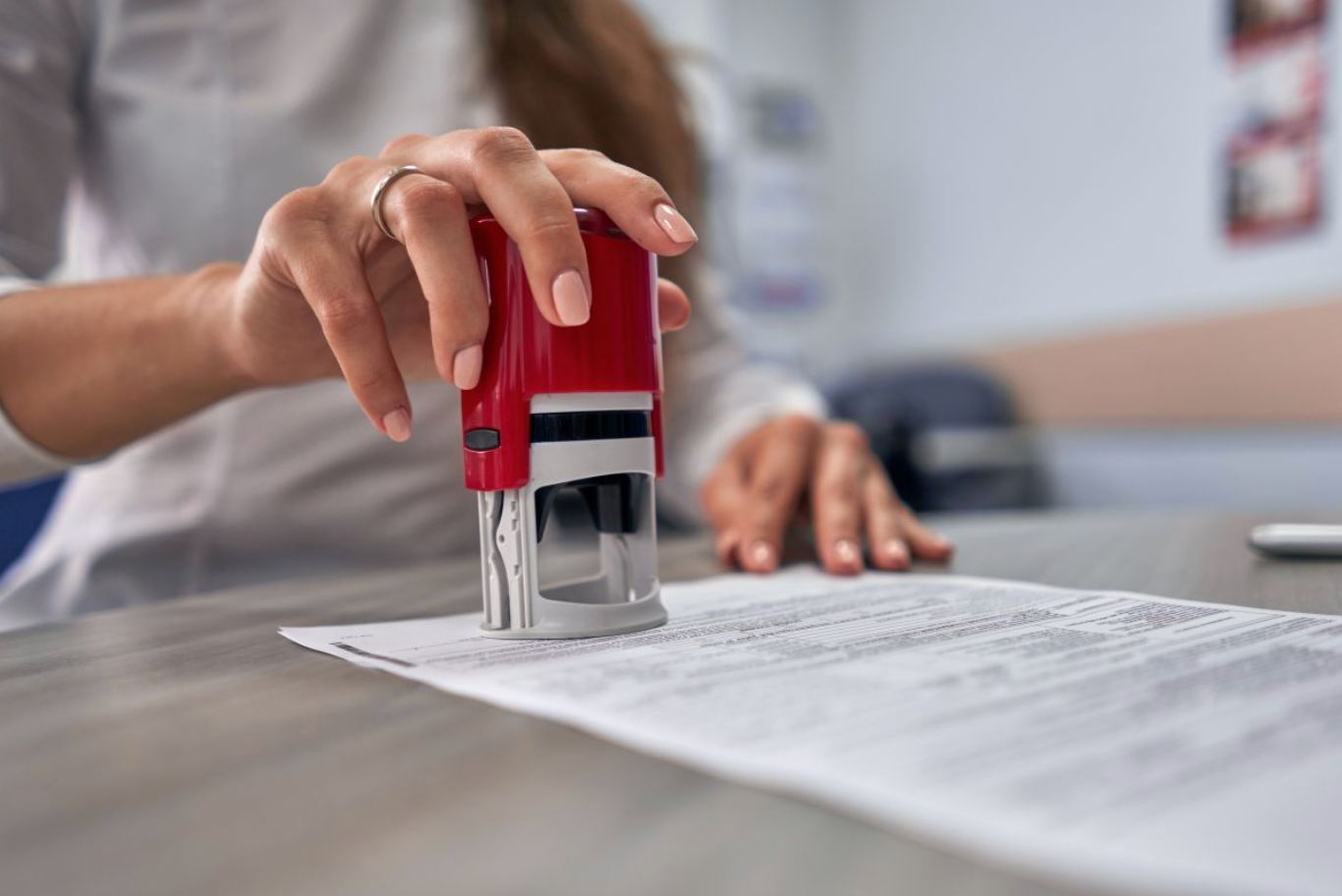 Iemand gebruikt een rode zelfinktende stempel op een document dat op een houten bureau ligt.